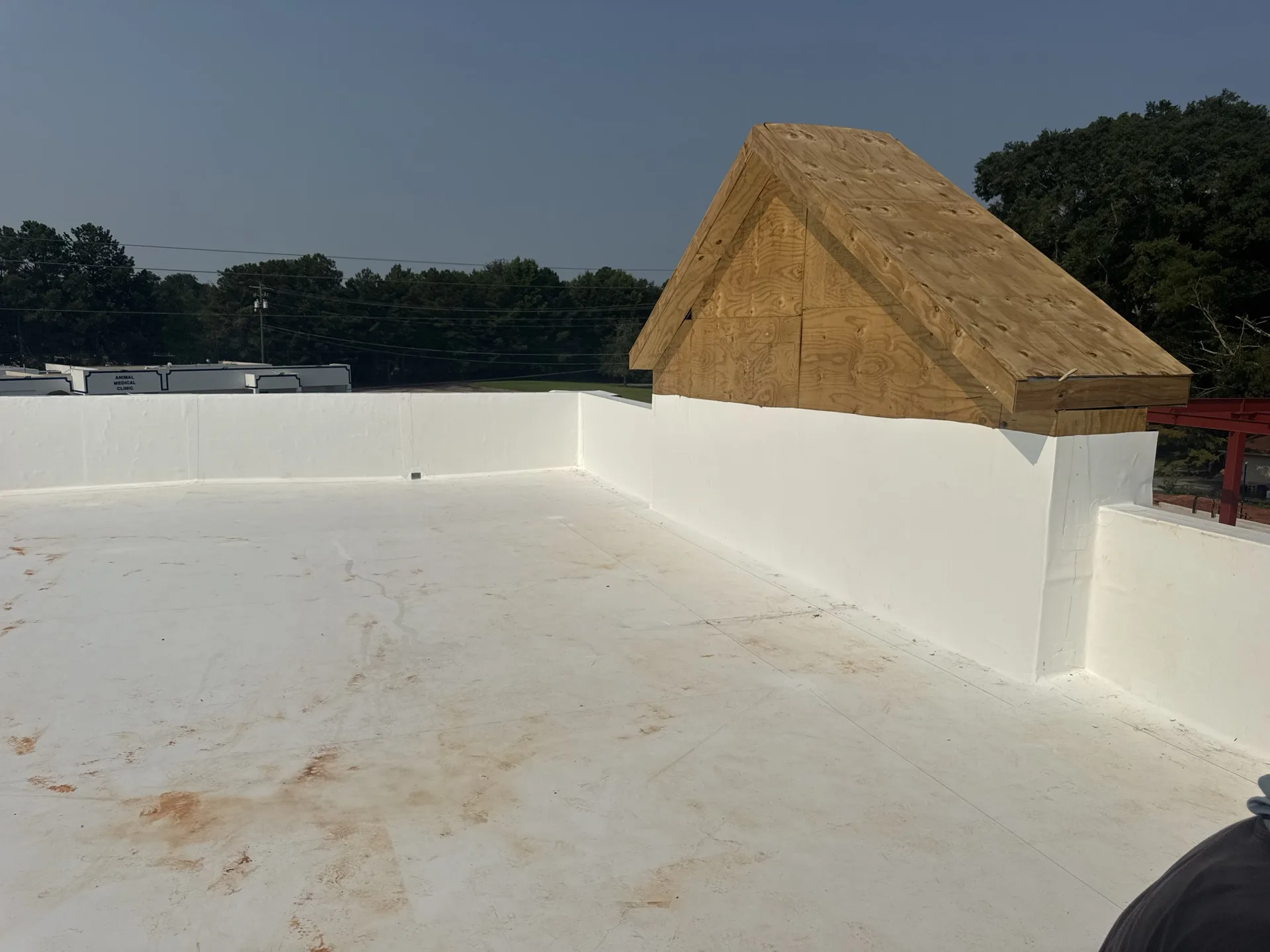 White low-slope roof membrane carried up parapet walls beside an unfinished plywood-clad roof feature